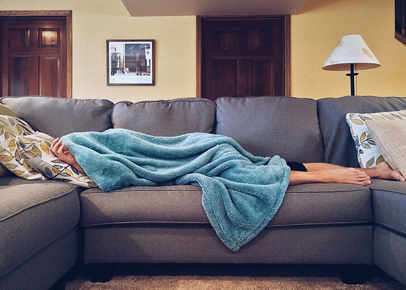 Person sleeping on couch with blanket covering them